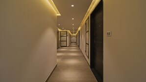 A modern hotel corridor with recessed lighting, a tiled floor, and a dark-colored elevator door. - Treebo Pink City Grand (Jaipur)