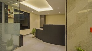 A modern reception area with a curved desk, a potted plant, and a glass wall. - Treebo Pink City Grand (Jaipur)