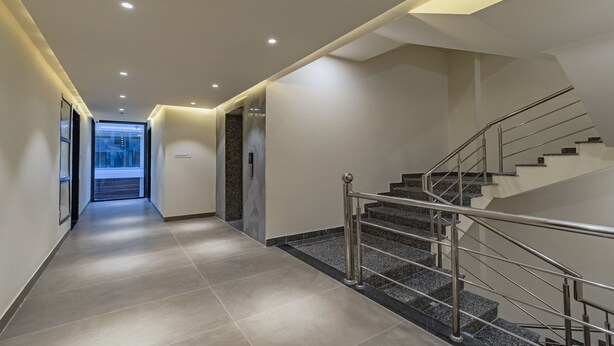 A modern hotel hallway with a staircase, tiled flooring, and a glass door leading outside. - Treebo Pink City Grand (Jaipur)