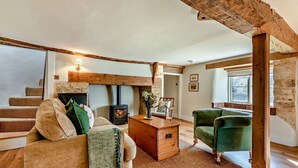 Una sala de estar acogedora con chimenea, un sofá, un sillón verde y una escalera de madera.