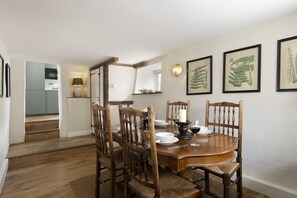 Un comedor con mesa y sillas de madera, impresiones botánicas enmarcadas en la pared y una cocina al fondo.