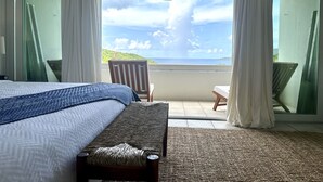 Una camera da letto con un letto, una panca, una sedia e vista sull'oceano.