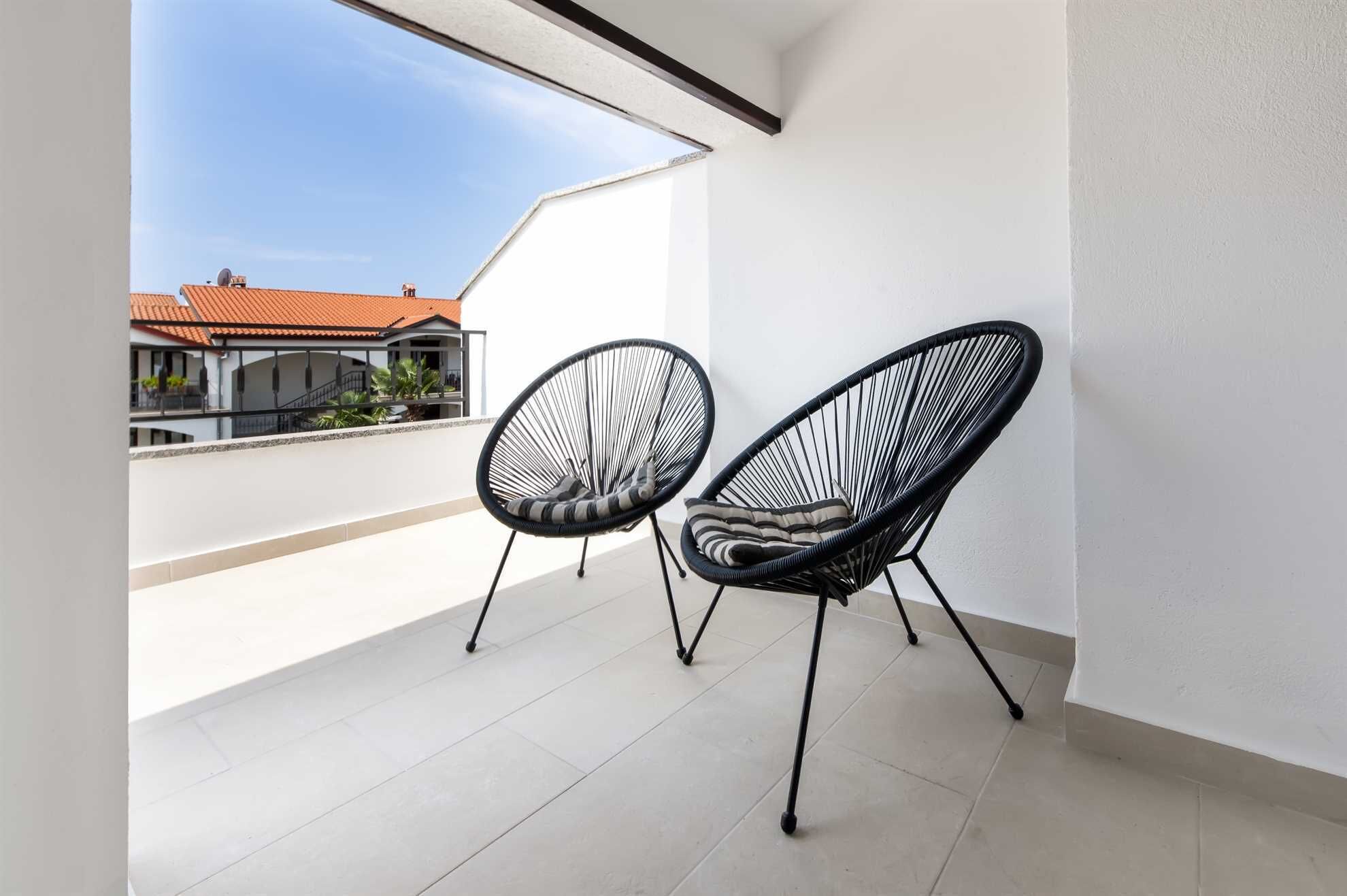 A balcony with two black wire-framed chairs and a white tiled floor.