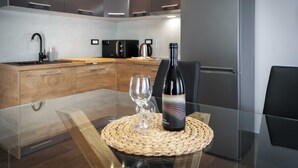 A modern kitchen with a glass dining table, a woven placemat, a wine bottle, and a wine glass.