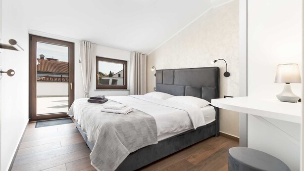 A modern bedroom with a bed, a bedside table, a lamp, and a view of the outside.