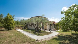 Einbungalow mit einer hellbeigen Fassade, einem roten Ziegeldach und einer kleinen Terrasse mit Tisch und Stühlen.