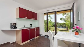 Eine moderne Küche mit roten Schränken, einer Kaffeemaschine und Blick auf einen Garten durch große Schiebetüren.