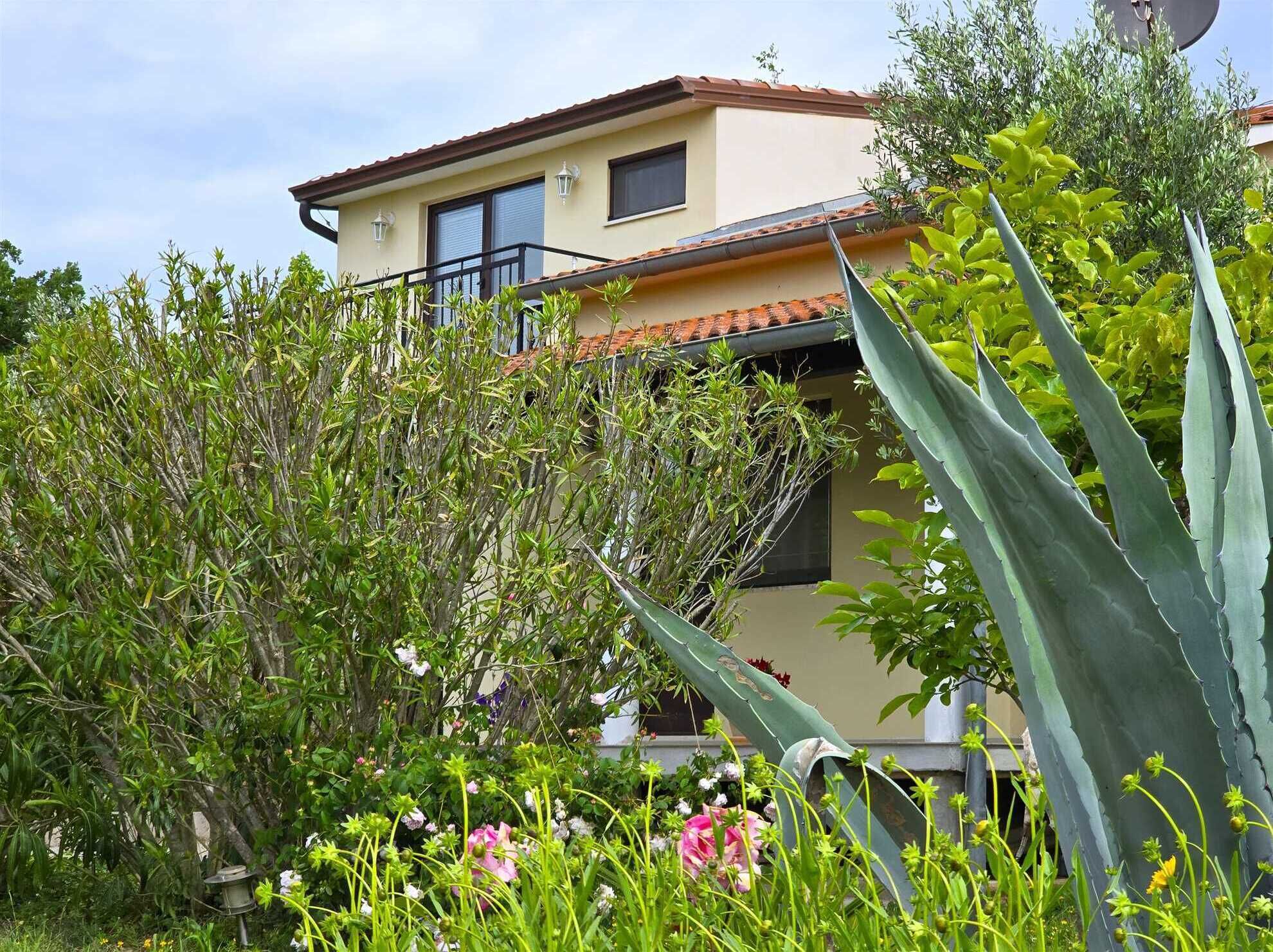 Une maison à deux étages dotée d’un balcon, entourée de différentes plantes et fleurs.