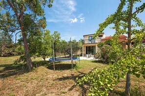 Um imóvel residencial com um trampolim no quintal, cercado por árvores e uma casa com varanda.