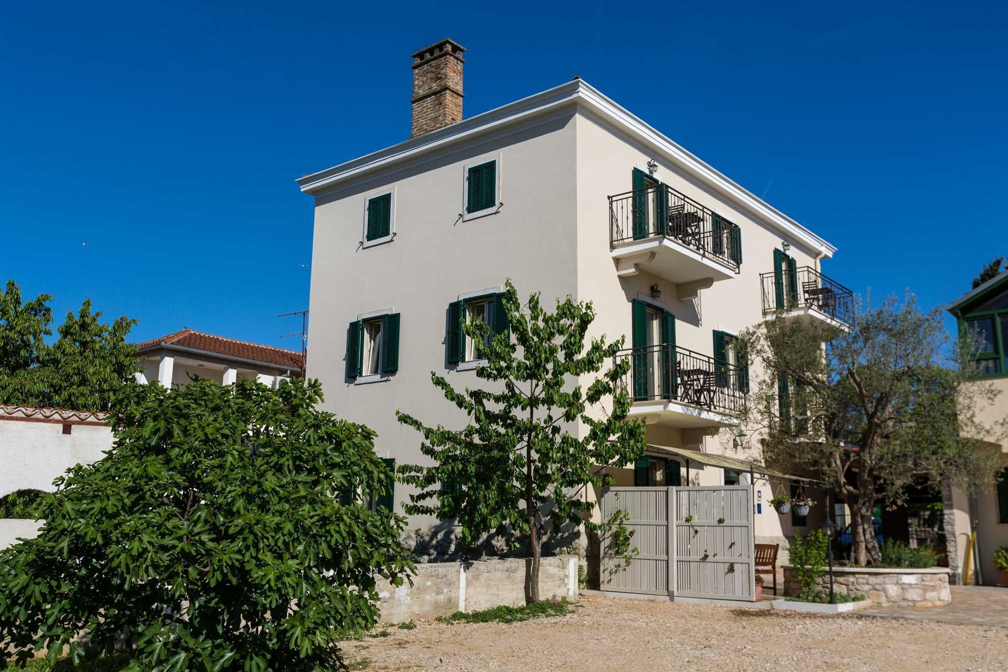 A two-story building with a balcony on the second floor, a gated entrance, and surrounding greenery.