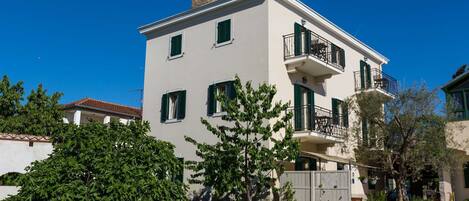 A two-story building with a balcony on the second floor, a gated entrance, and surrounding greenery.