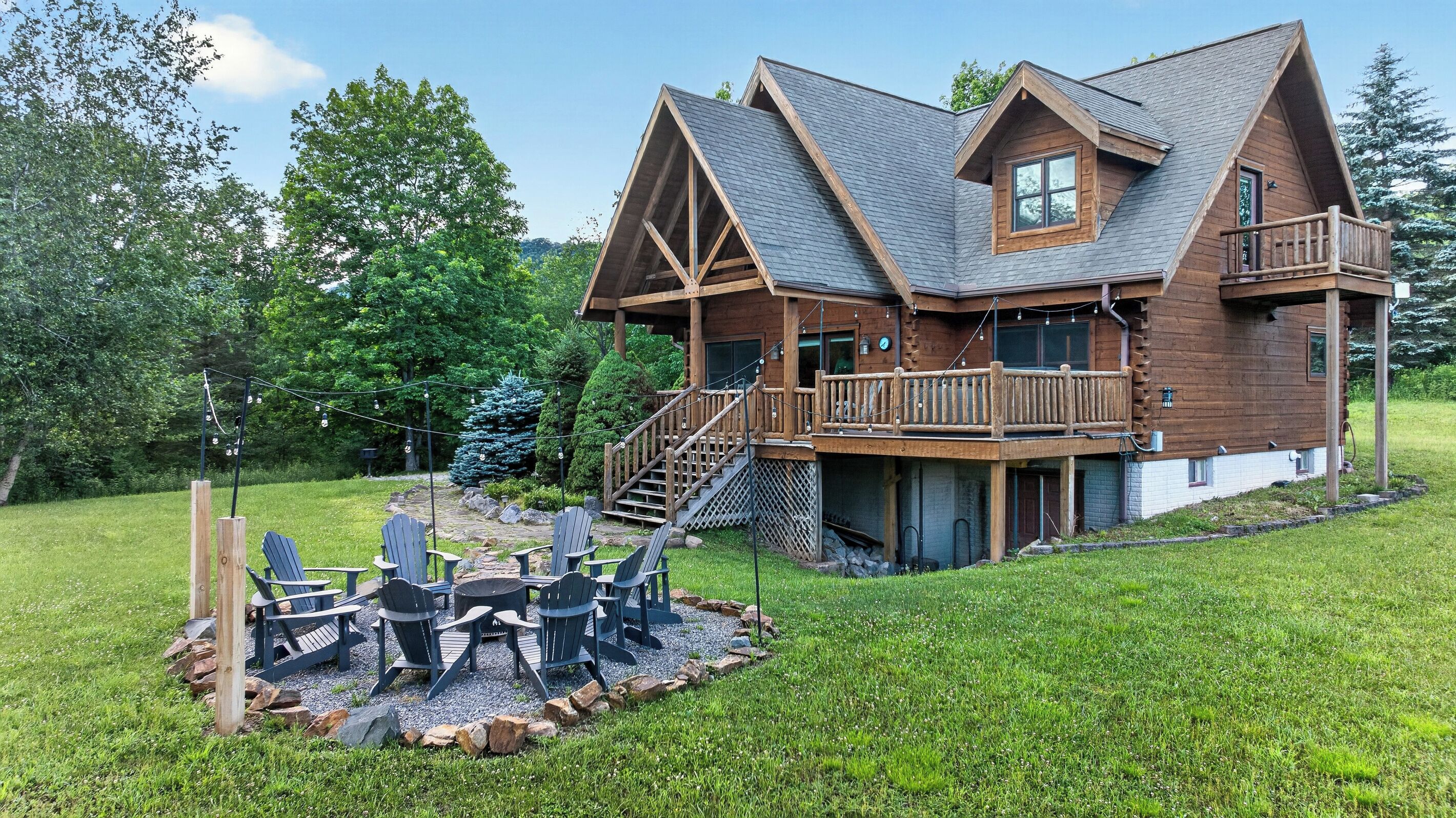 A wooden cabin with a deck, outdoor seating, and a stone fire pit.