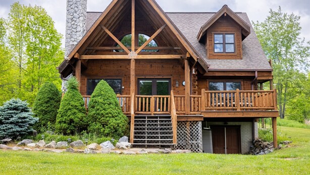 A log cabin with a prominent gable roof, a stone chimney, and a wooden balcony. - Log Cabin near Snowshoe | Hot Tub + Mtn Views | 5 Wooded Acres (Slatyfork)