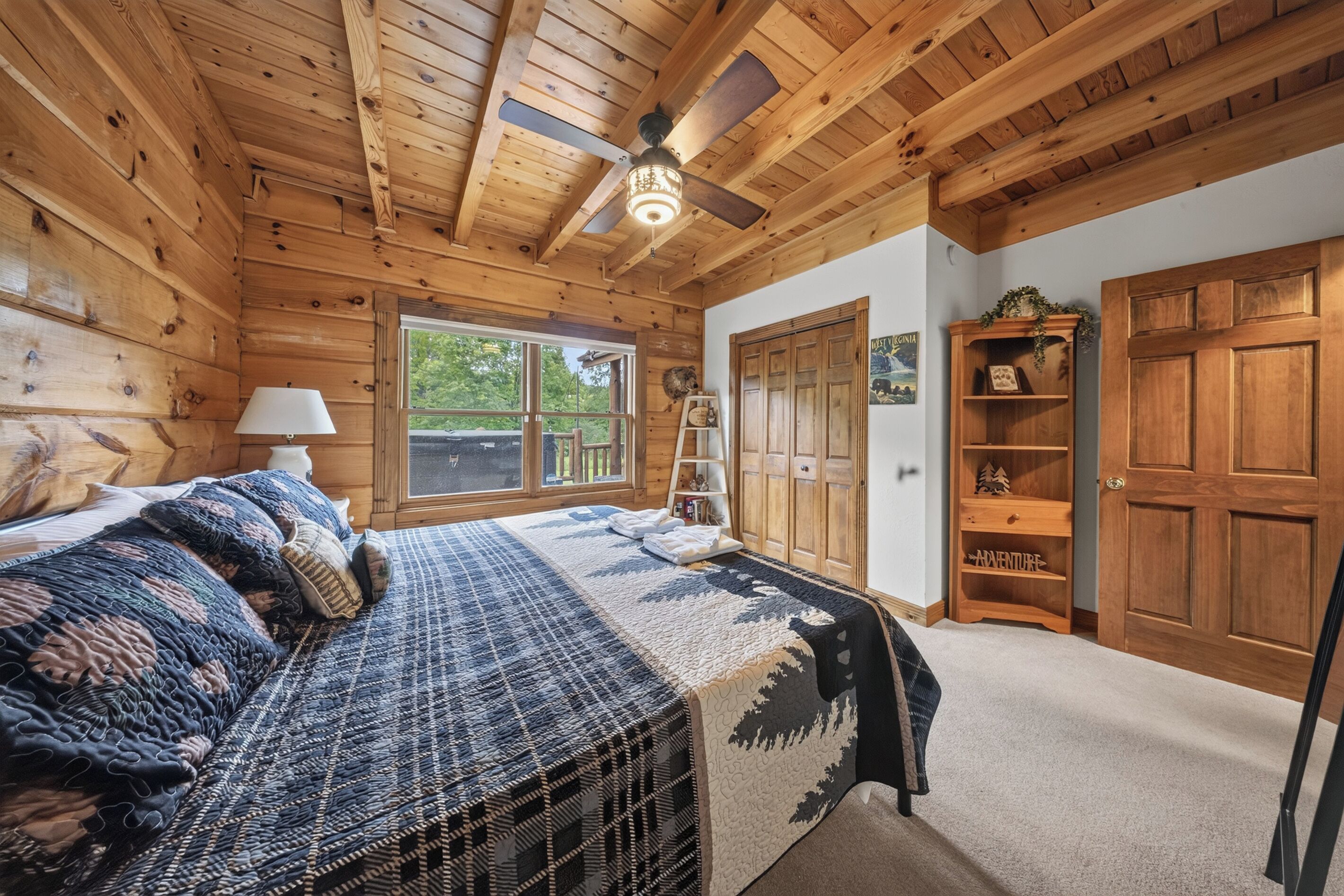 Une chambre dans une cabane en bois, avec un lit, un ventilateur de plafond, une fenêtre et une porte en bois.