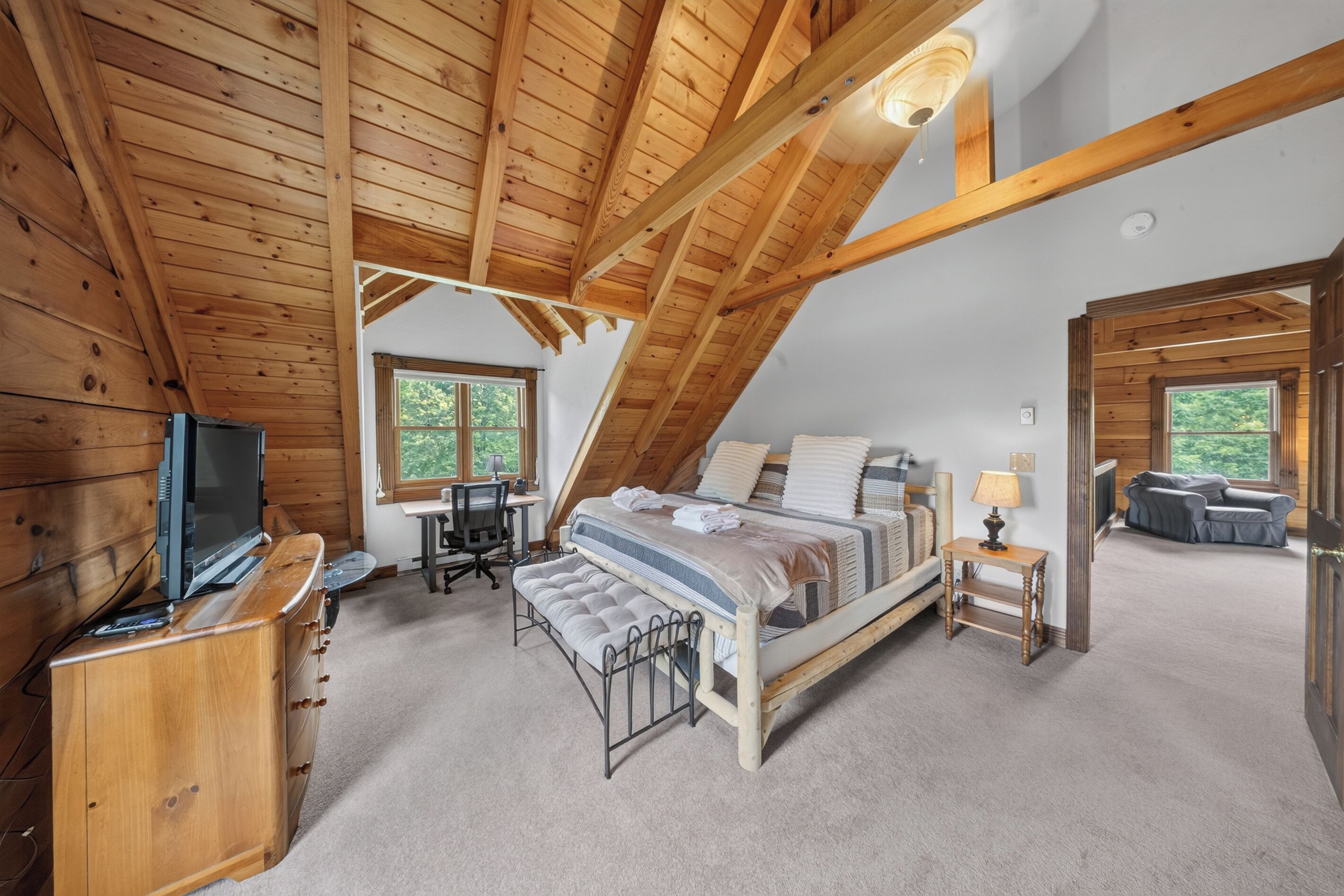 A loft-style bedroom with a sloped ceiling, a bed, a desk, a television, and a window.