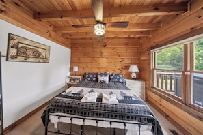A wooden cabin bedroom with a bed, nightstands, a ceiling fan, and a window with a view.