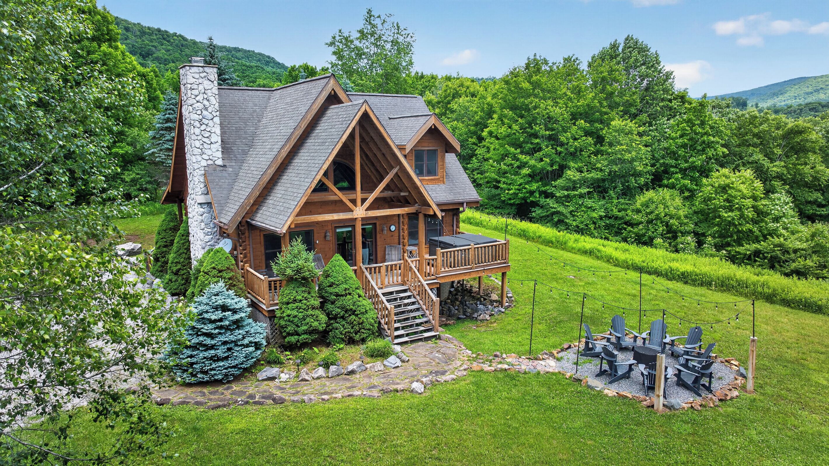 A log cabin with a stone chimney, wooden deck, and a stone pathway leading to the entrance.