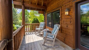 A wooden deck with rocking chairs and a large window overlooking a forested area. - Log Cabin near Snowshoe | Hot Tub + Mtn Views | 5 Wooded Acres (Slatyfork)