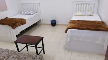 A small, clean room with two single beds, a small table, and a patterned sofa.