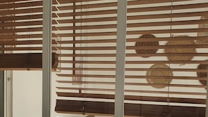 Una habitación con una cama, una ventana con persianas de madera y una cesta tejida.
