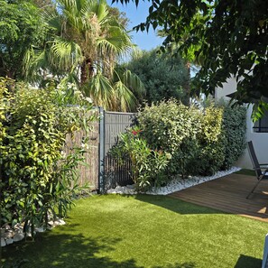 Un jardín bien cuidado con diversas plantas, una terraza de madera y una reja de metal.