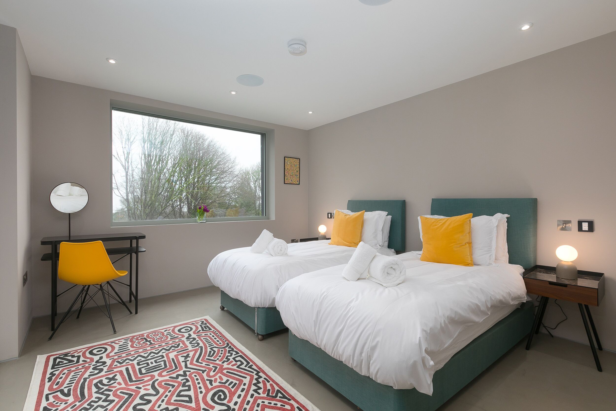 A modern hotel room with two beds, a desk, a chair, and a large window.