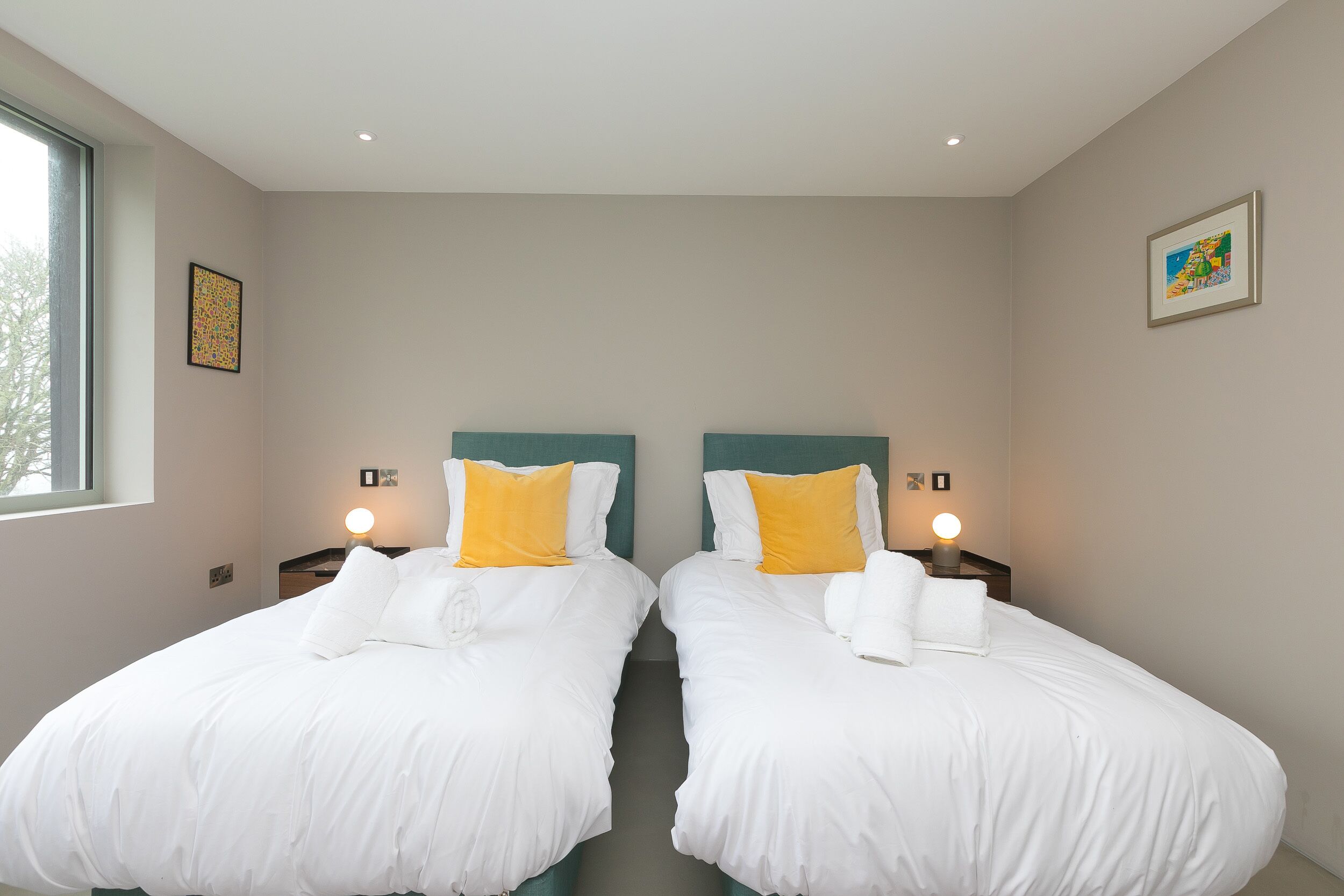 Une chambre d’hôtel avec deux lits simples, chacun doté de draps blancs et d’un oreiller jaune, et une petite table placée entre les deux.