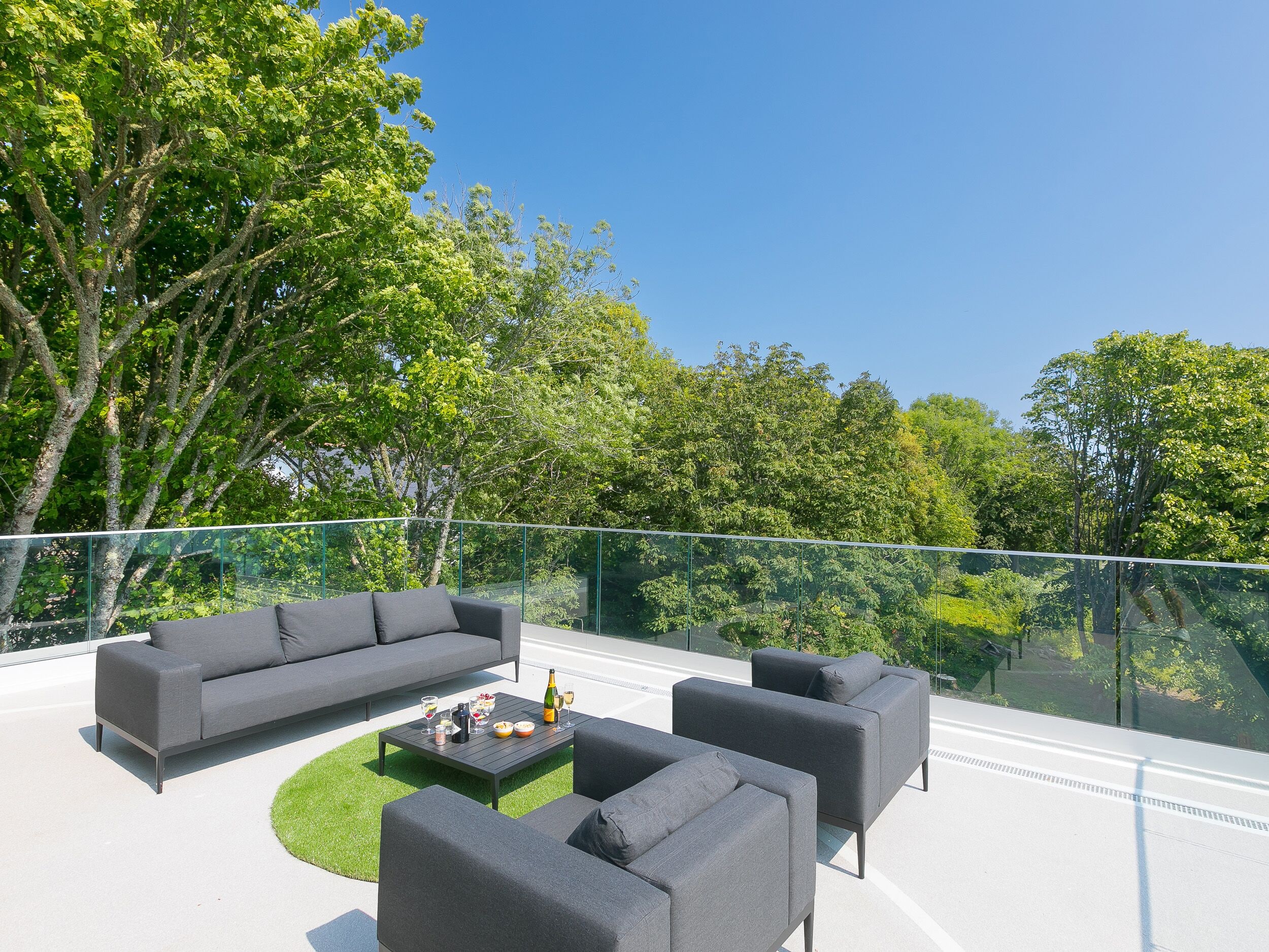 A modern outdoor seating area with a glass balustrade, a sofa, two armchairs, and a coffee table.