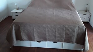 A single bed with a white frame and a brown blanket in a room with wooden flooring and white walls.