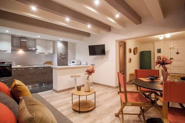 Une cuisine moderne dotée d’appareils électroménagers intégrés, un coin repas avec une table et des chaises, et un salon avec un canapé.
