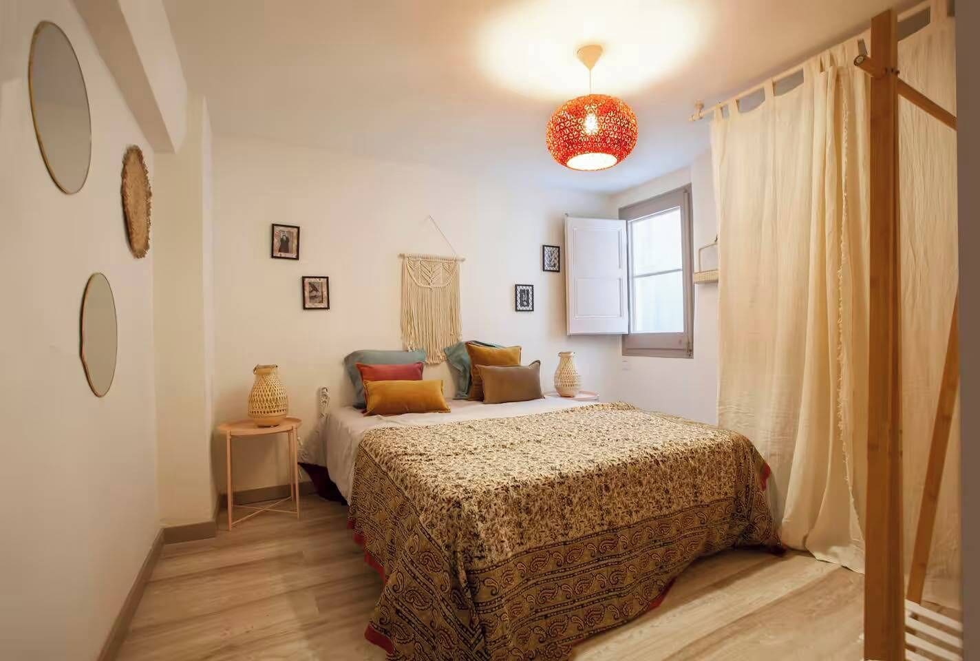 Een slaapkamer met een groot bed, een nachtkastje, een hanglamp en een raam met gordijnen.