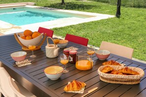 Colazione con croissant, succo d'arancia e diversi condimenti su un tavolo vicino a una piscina.