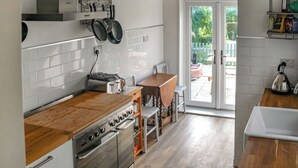 Moderni keittiö, jossa on valkoisilla laatoilla päällystetyt seinät, puutasot, ruostumattomasta teräksestä valmistetut kodinkoneet ja lasiliukuovi, joka johtaa ulkoterasille.