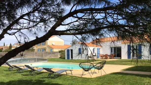 Una piscina con sillas de descanso, un patio y un edificio con tejado de baldosas.