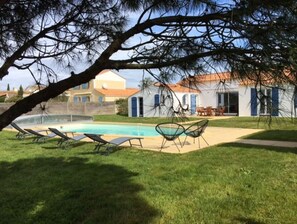 Une piscine avec des chaises longues, un espace patio et un bâtiment doté d’un toit en tuiles.