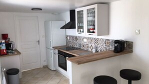 Una cocina compacta con armarios blancos, una campana extractora negra, un microondas y una cafetera. Hay dos taburetes negros y un salpicadero de azulejos.