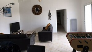 Una sala de estar con un sofá, una mesa de centro, un televisor y una mesa de futbolín.