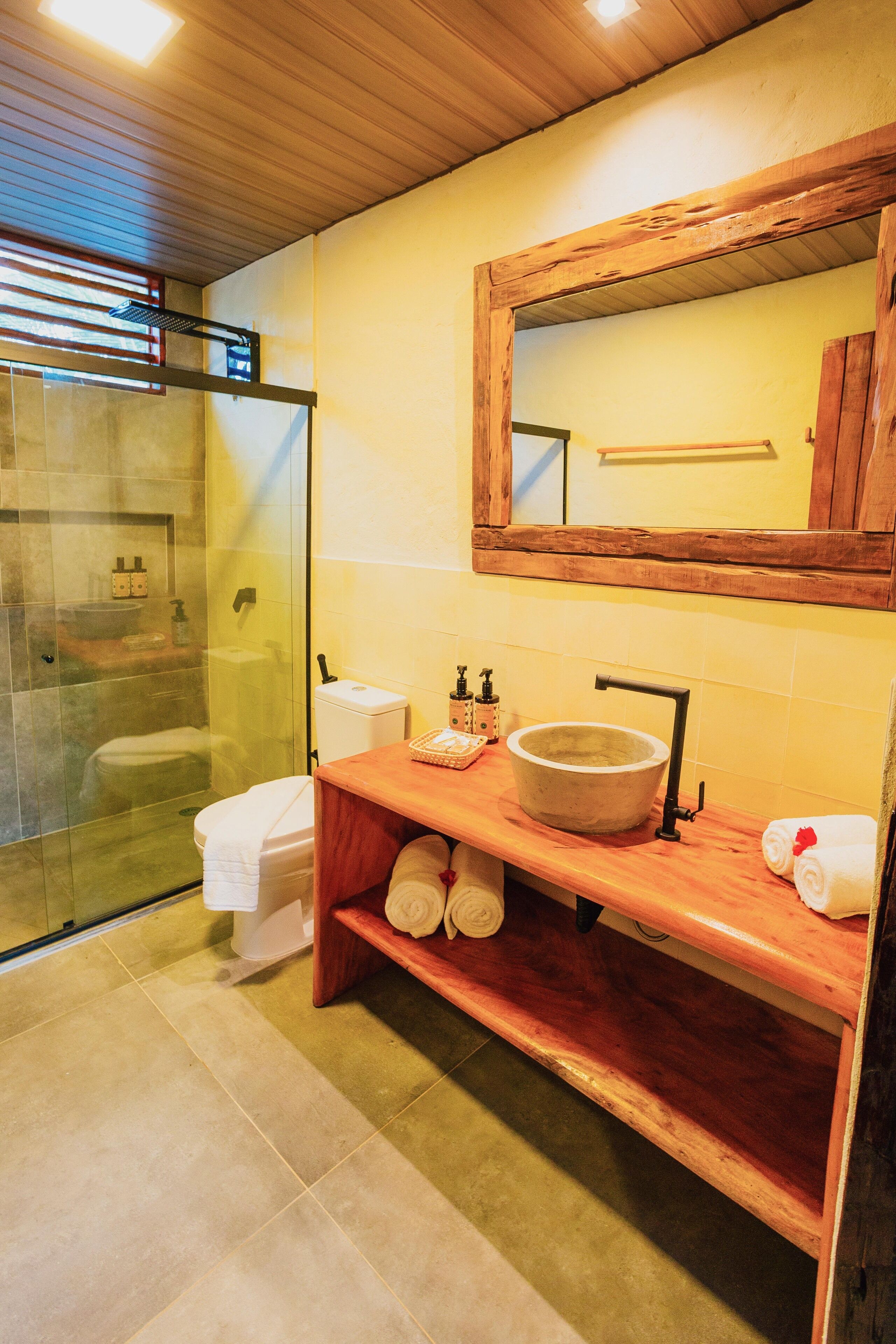Un bagno con box doccia in vetro, un mobile bagno in legno con un lavandino grande e uno specchio sopra il mobile.