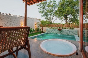 Un área de spa con una bañera de hidromasaje, una silla de madera y una pequeña piscina.