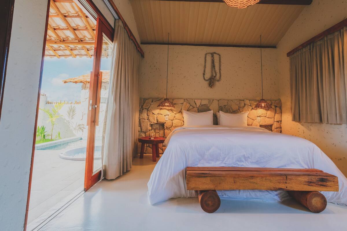 Camera con parete in pietra, un letto con una panca in legno e vista su una piscina.