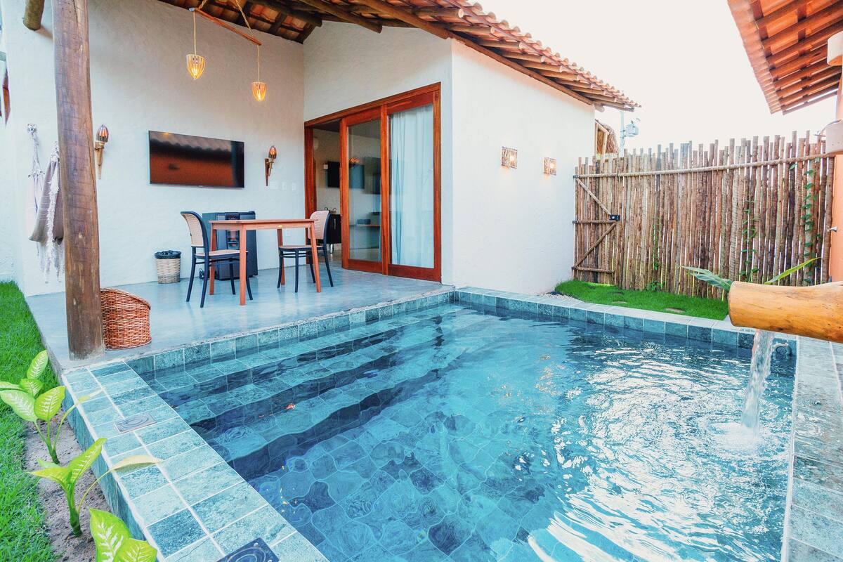 Una piscina con bordo piastrellato, una pergola in legno e un'area pranzo con tavolo e sedie.