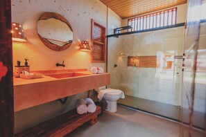 Un baño moderno con tocador de madera, un espejo redondo y mampara de ducha de vidrio.