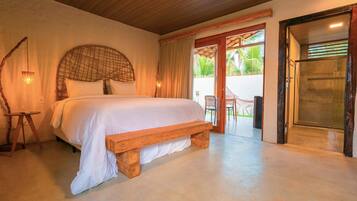 Un dormitorio con una cama grande, cabecera de madera y un banco. Se ve una puerta que da a un espacio exterior con una silla y una mesa.
