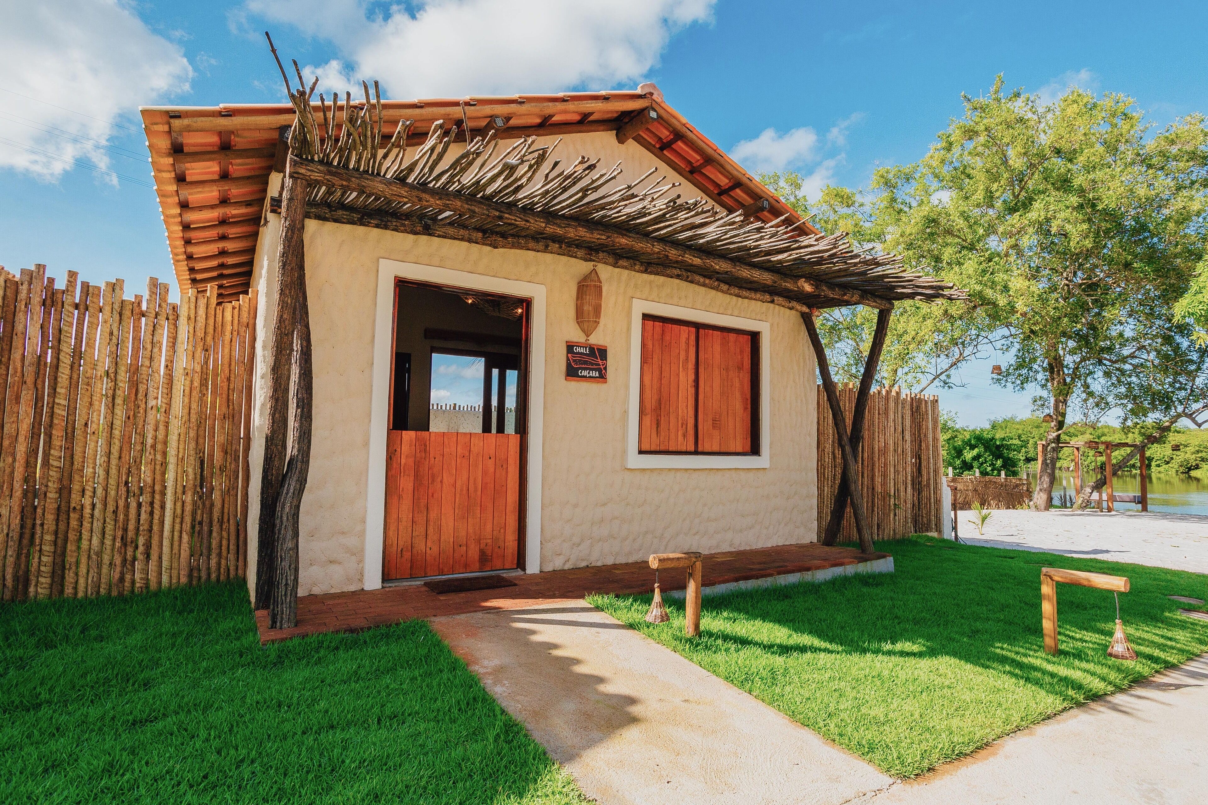 A small building with a wooden door and windows, surrounded by a wooden fence and a grassy area.