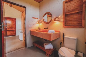Un baño con tocador de madera, lavamanos, inodoro y espejo.