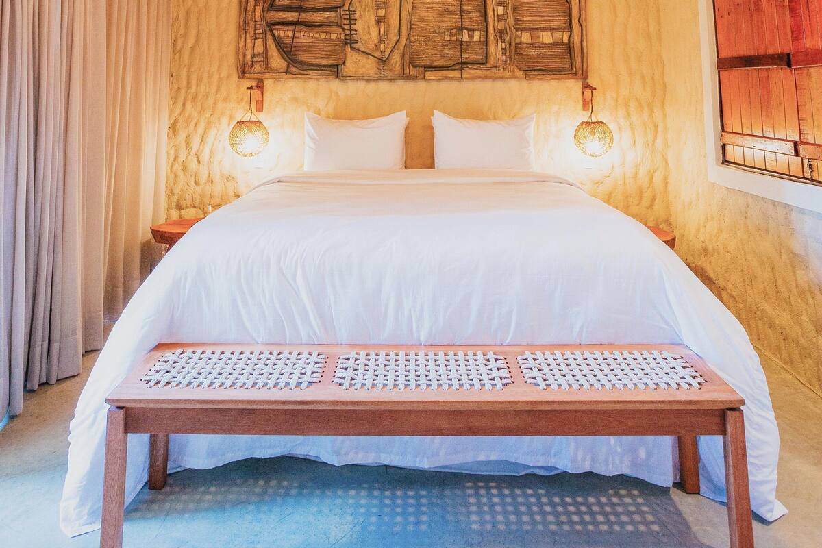 Una camera da letto con soffitto in legno, un letto con biancheria da letto bianca, un divano a capos letto e un lampadario a parete.