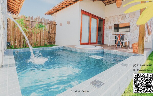 Una piscina con cerca de bambú, pared de piedra y zona de terraza con baldosas y mobiliario de exterior.
