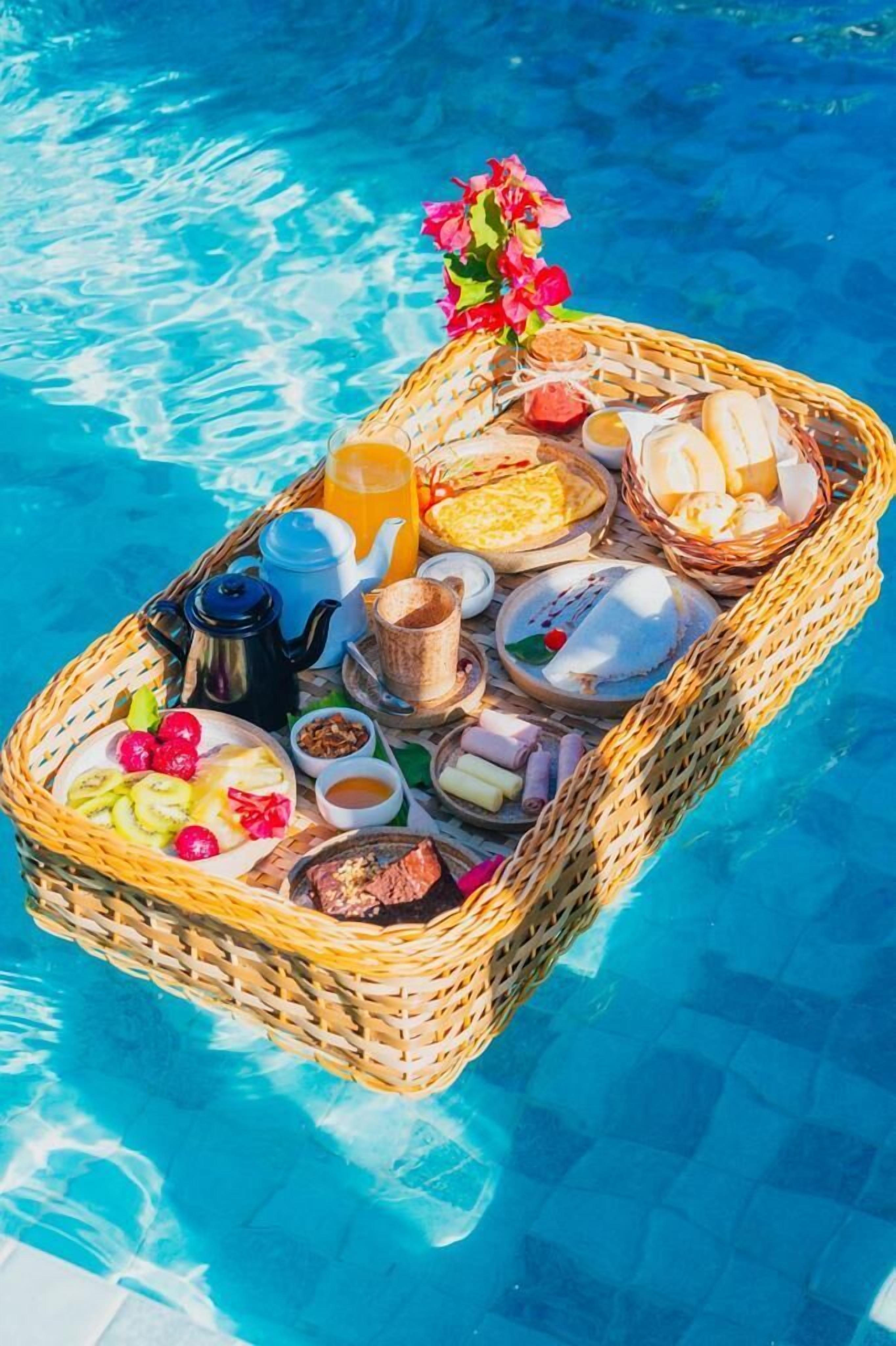 Uma cesta flutuante com itens de café da manhã sobre uma piscina.