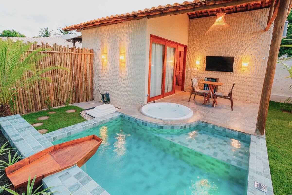 Area piscina privata con idromassaggio, un solarium in legno e una zona salotto con tavolo e sedie.