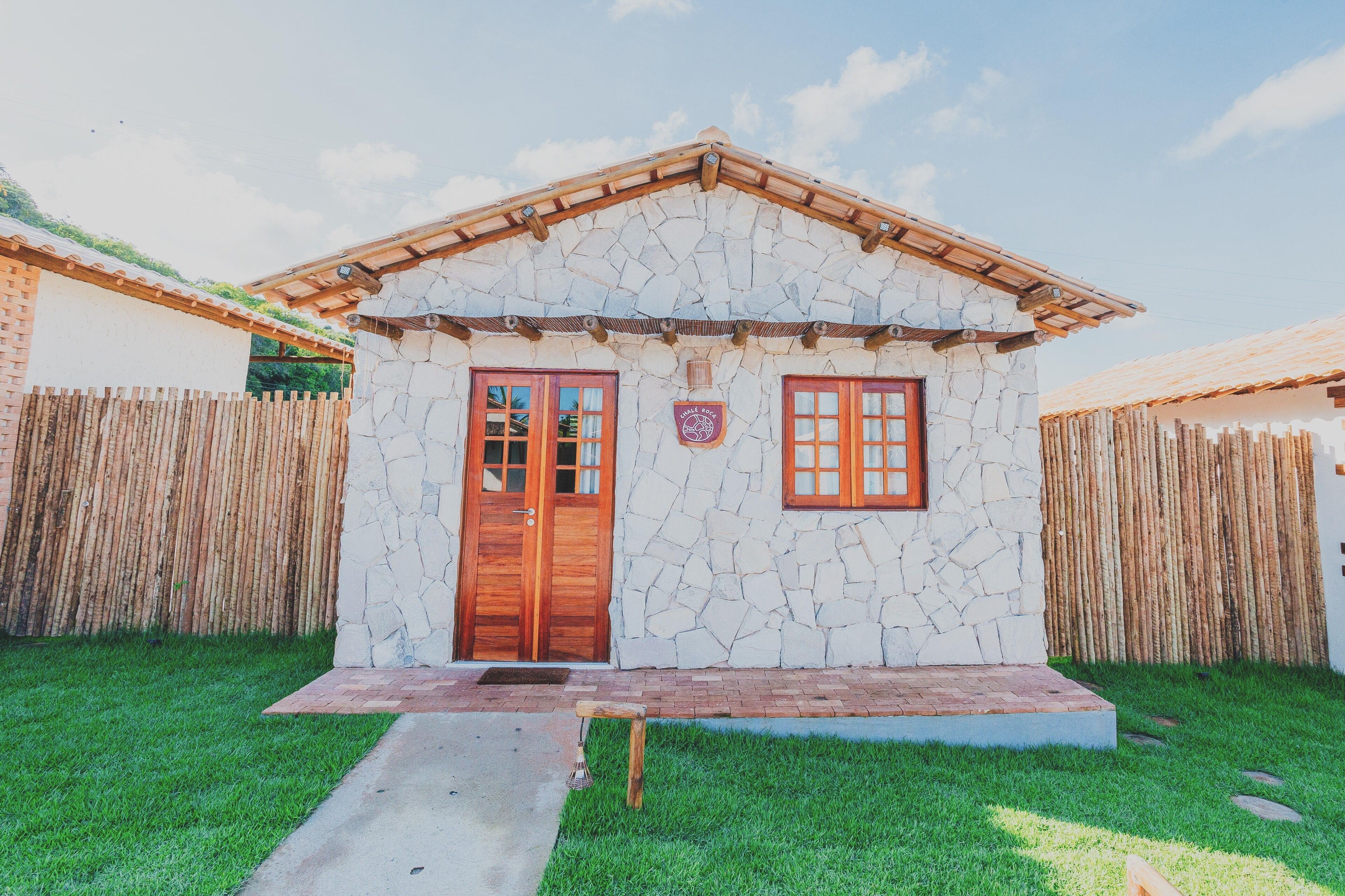 Una casa de piedra con puerta y ventanas de madera, rodeada por una cerca de bambú.